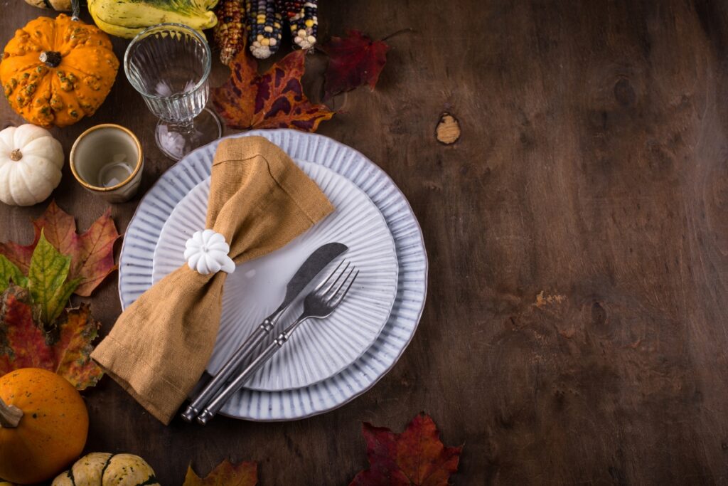 Fall party table setting with napkin, fork, knife and pumpkins.