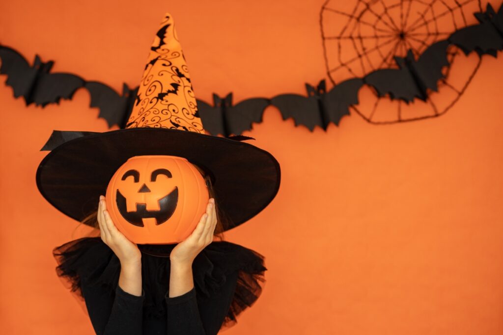 girl with witch hat holding a jack-o-lantern to her face