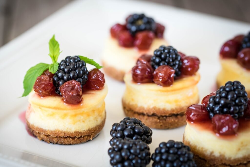 Dessert catering with cheesecakes topped with blackberries and mint on a white plate.