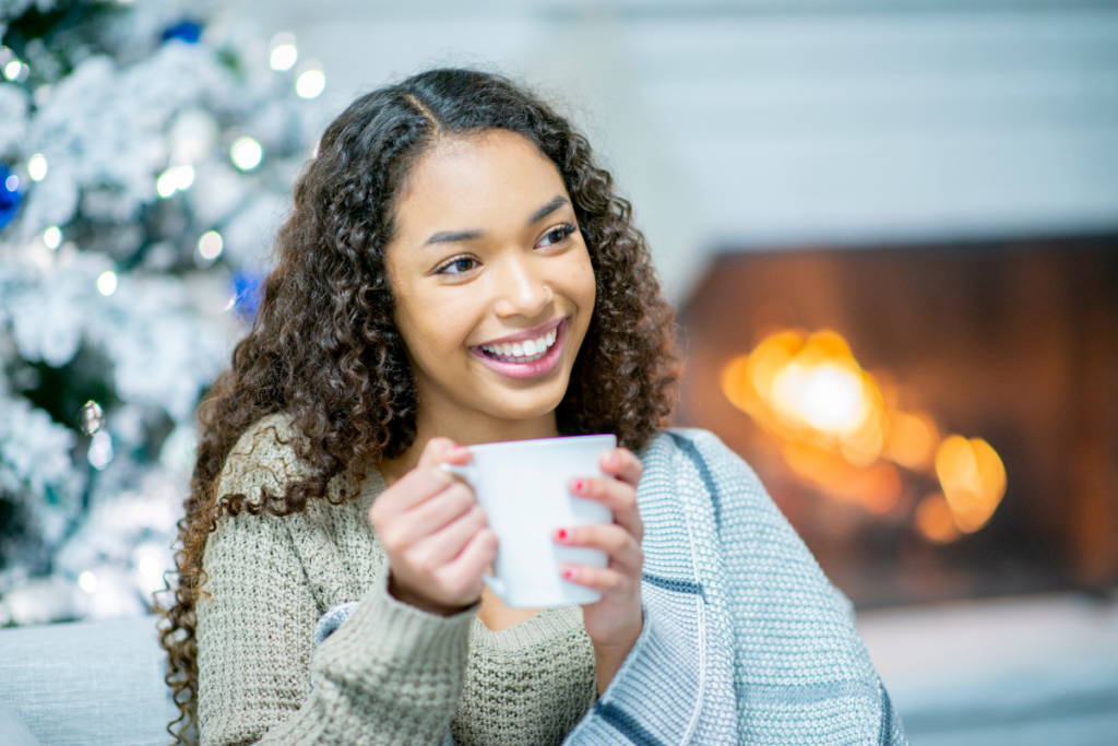 A young woman holding a cup of hot cocoa in front of a Christmas tree.