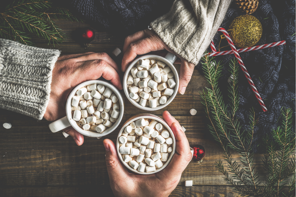 Hot Cocoa Party Ideas: Two hands holding mugs of hot cocoa with marshmallows.