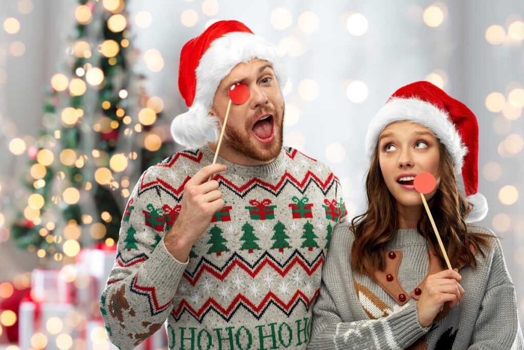A couple in santa hats holding a christmas stick in front of a christmas tree.