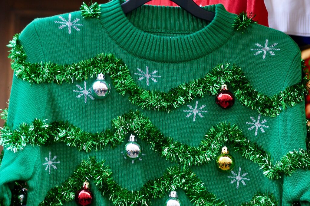 A green ugly Christmas sweater with ornaments hanging on a hanger for an ugly sweater party.