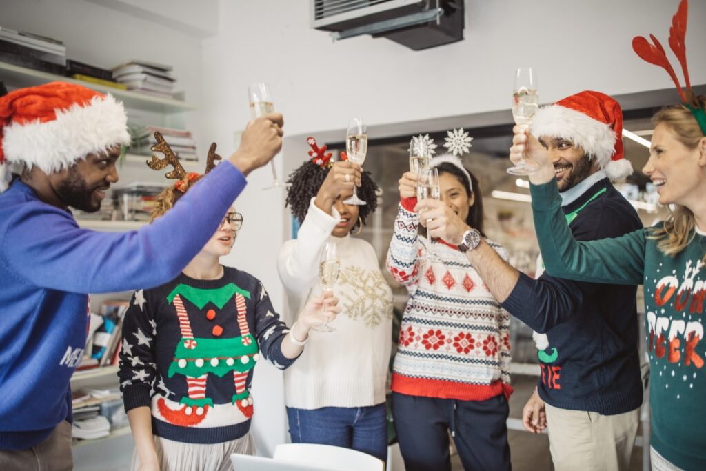 A group of people in ugly sweaters toasting in an office during a Christmas celebration.