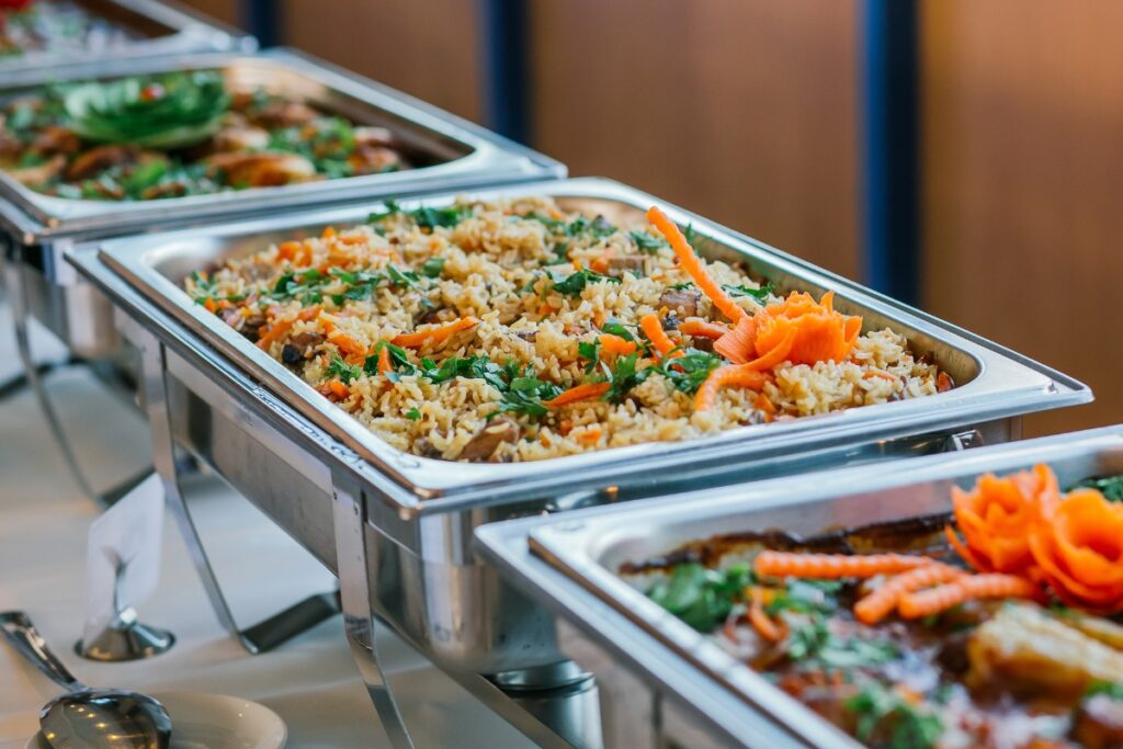 A row of silver trays with plant-based food in them.