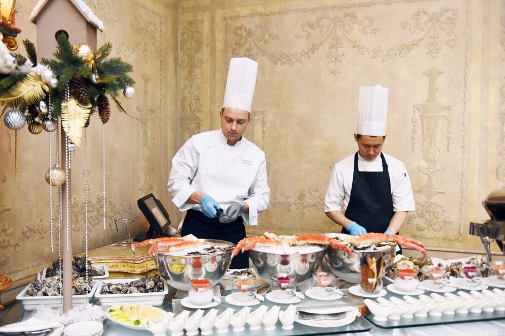 Two chefs efficiently preparing food at a buffet table for a catering event.
