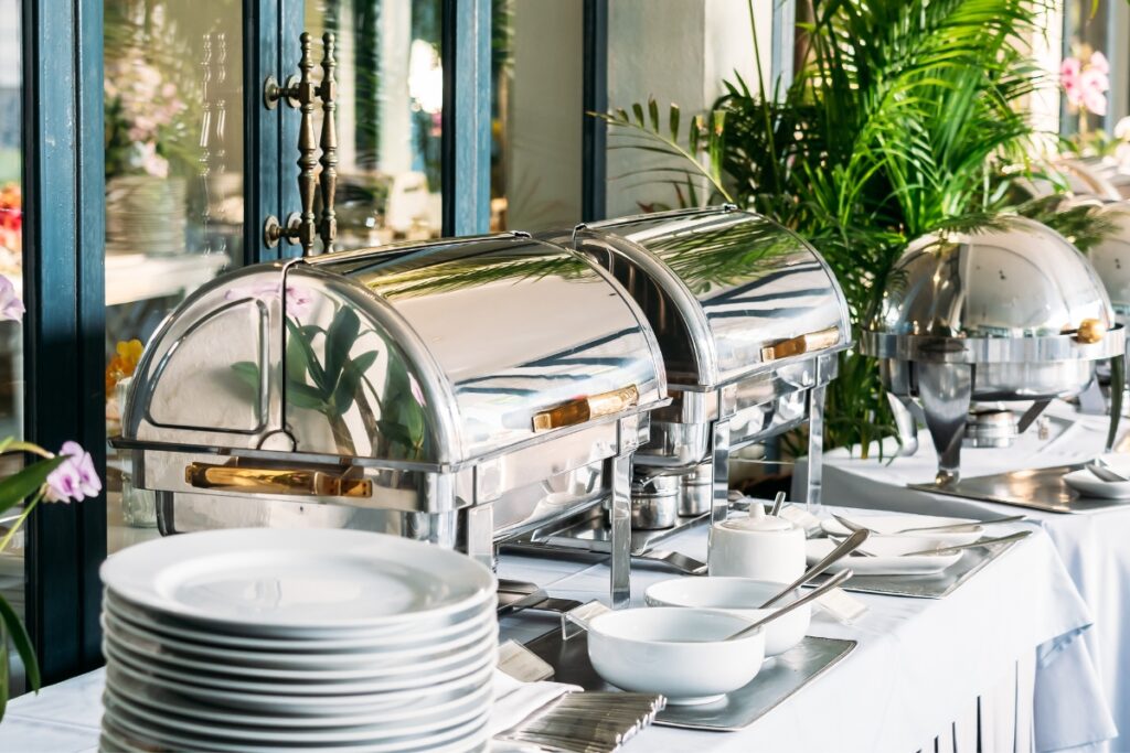 A buffet table with elegant silver utensils and plates, offering a variety of scrumptious dishes for catering.