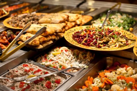 A buffet spread featuring a variety of salads, vegetables, and breaded fish, served in large, elegant dishes at event food stations with serving utensils.