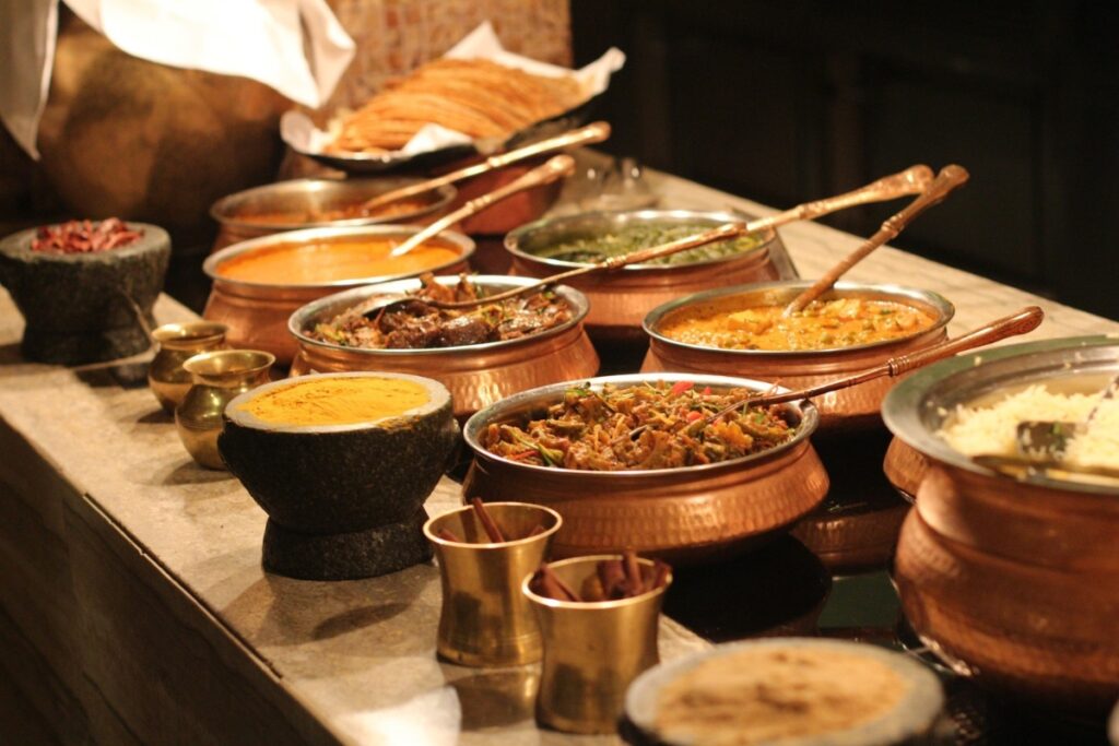 Assorted Indian dishes served at event food stations in traditional bowls on a buffet table, featuring curry, rice, and bread.