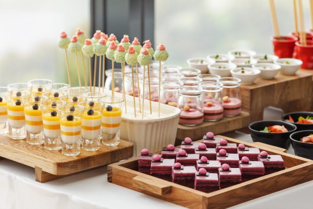 An elegant event food station with assorted desserts including layered parfaits, cake pops, and a layered red cake with small round toppings.