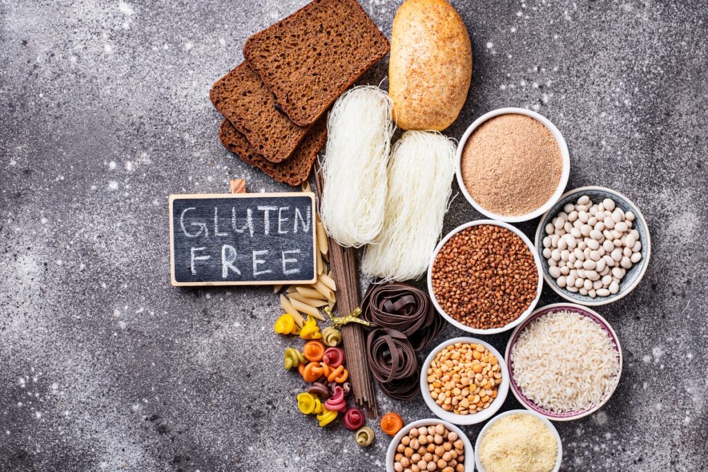 Various gluten-free foods arranged on a textured surface, including pasta, bread, rice, legumes, and a "Gluten Free" sign on a small chalkboard, ideal for gluten free catering events.