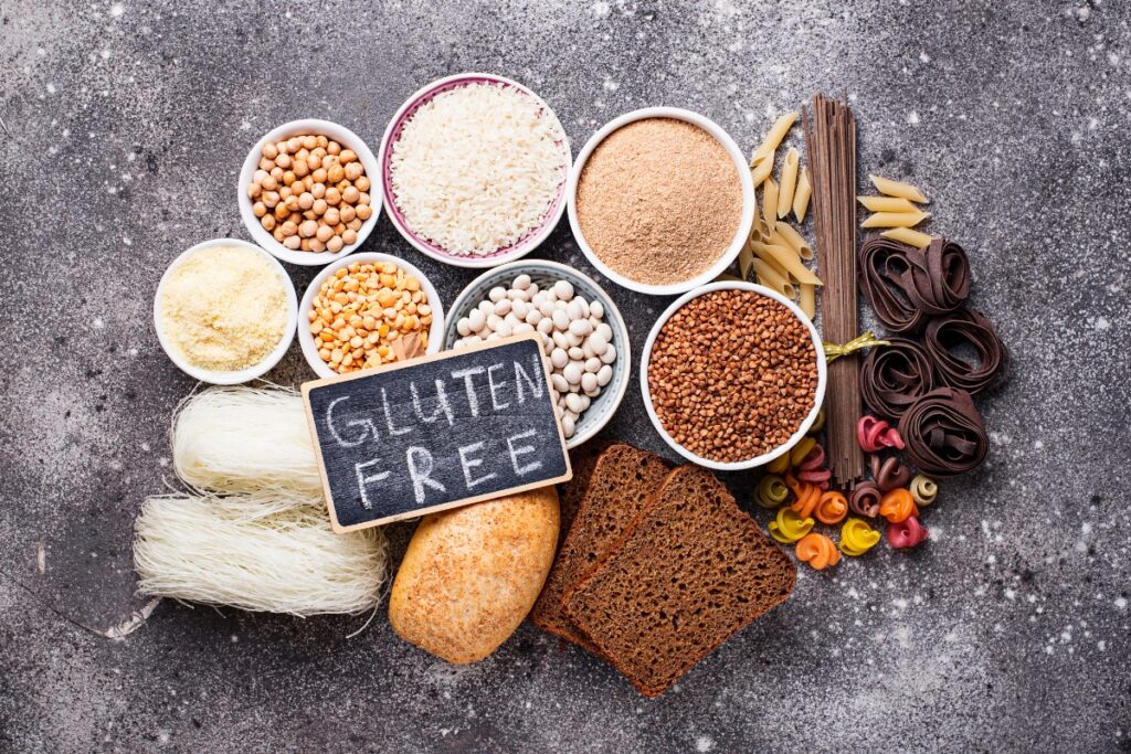 An assortment of gluten-free foods, including various grains, pasta, breads, and legumes, elegantly arranged on a table with a small chalkboard sign that reads "GLUTEN FREE," perfect for gluten free catering events.