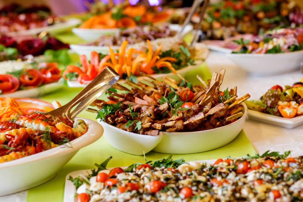 A buffet table with a variety of healthy catering options including salads, grilled vegetables, and meat skewers.