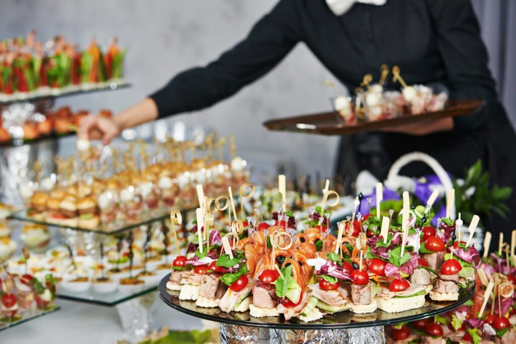 A waiter arranging a variety of healthy gourmet appetizers on a buffet table at a formal event.