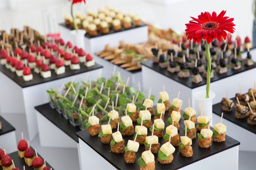 Assorted healthy appetizers neatly arranged on black pedestals with a red flower decoration at a catering event.