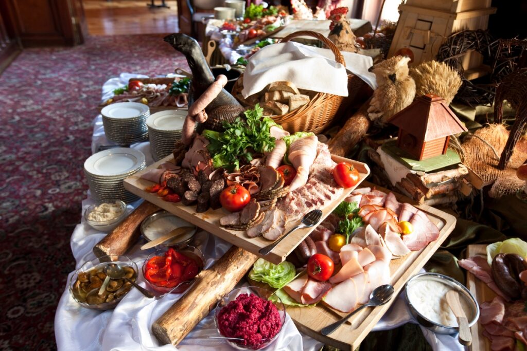 Lavish buffet spread featuring an assortment of healthy meats, cheeses, breads, and condiments on a wooden table in an elegant dining room.