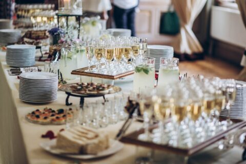 A buffet table with plates, various appetizers, desserts, and glasses filled with champagne, lemonade, and vibrant mocktails.