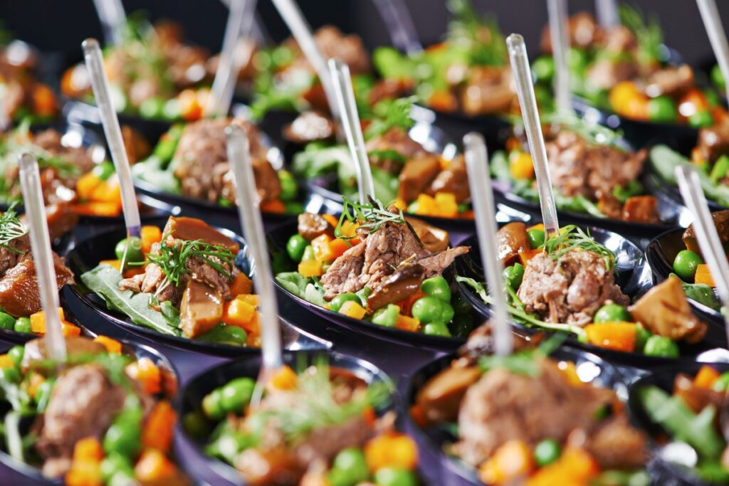 Rows of small, spoon-sized appetizers containing mixed vegetables and meat garnished with herbs—a perfect choice when considering catering tips for large groups.