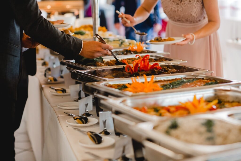 People serving themselves from a buffet with various dishes displayed in chafing dishes, showcasing some excellent catering tips for large groups.