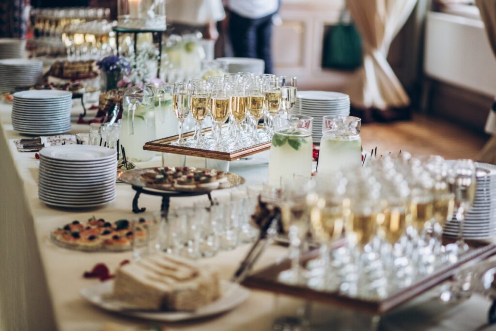 A buffet table is set with plates, glasses of champagne, pitchers of lemonade, and a variety of appetizers and desserts—excellent examples of catering tips for large groups.