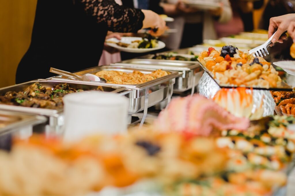 A buffet table filled with various dishes, provided by our custom catering services, with people serving themselves from the trays of food.