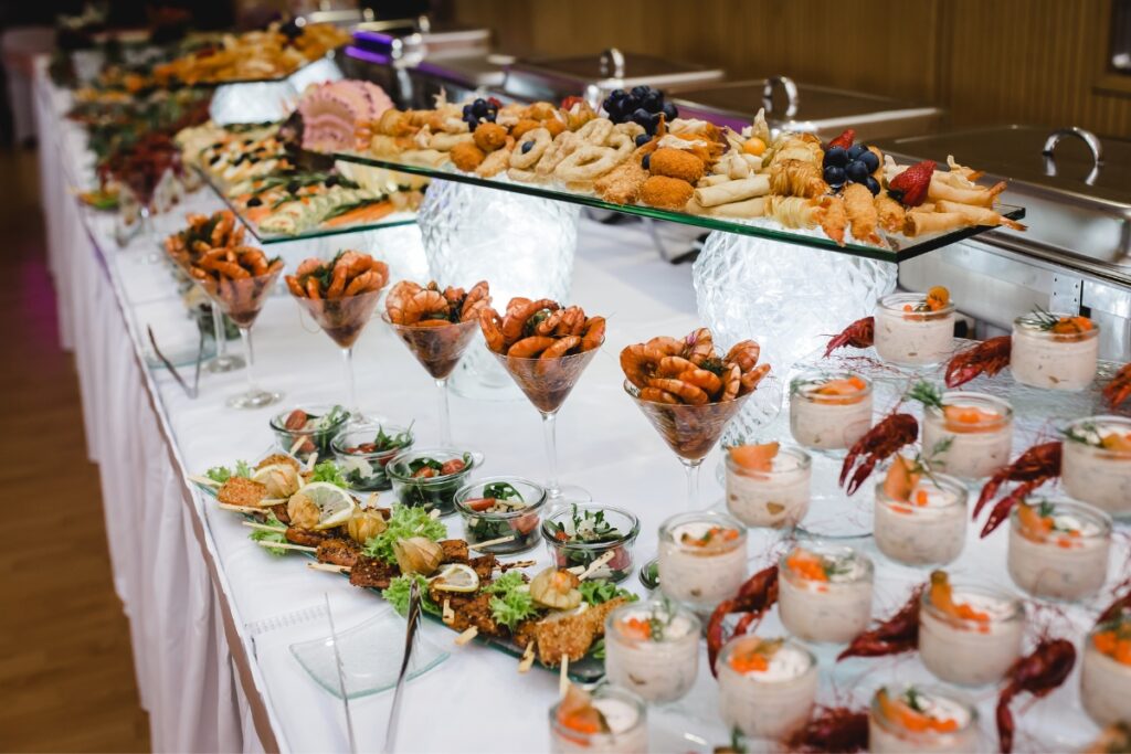 A buffet table arranged with various appetizers, including shrimp cocktails, breaded snacks, salads in glasses, and small servings of seafood, organized in an elegant display for an event by our custom catering services.