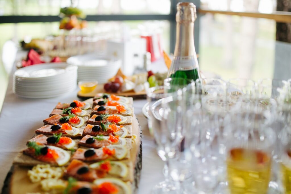 A table is set with a variety of appetizers, a bottle of champagne, empty glasses, and plates ready for a gathering, showcasing the expertise of our custom catering services.