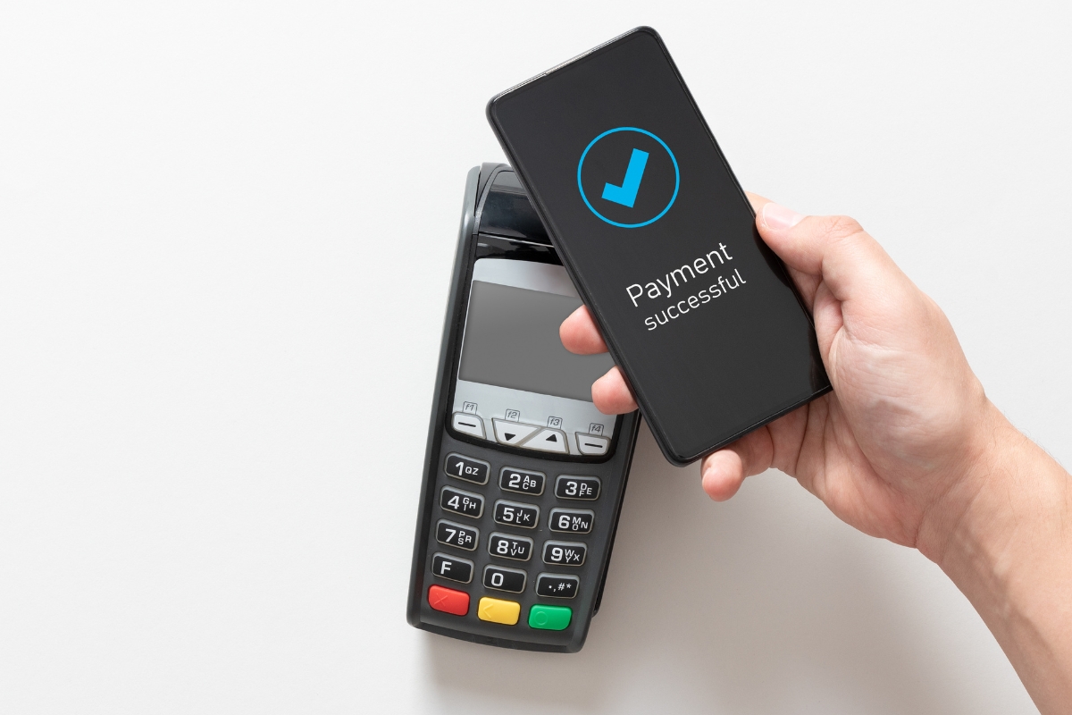 A hand holds a smartphone displaying "Payment successful" over a payment terminal, showcasing the seamless integration of catering technology.