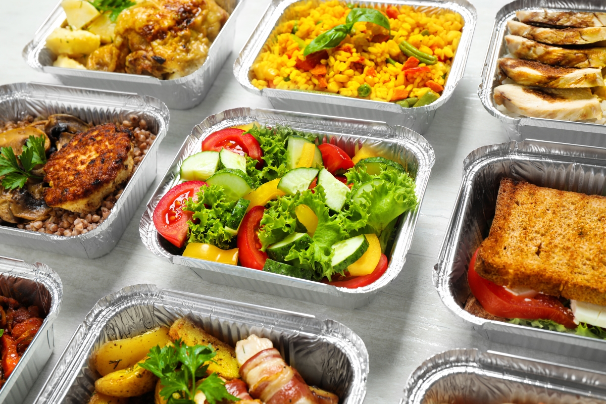 Assorted aluminum trays filled with various dishes, including salad, rice, vegetables, and meats, arranged on a white surface—perfect for office catering solutions.