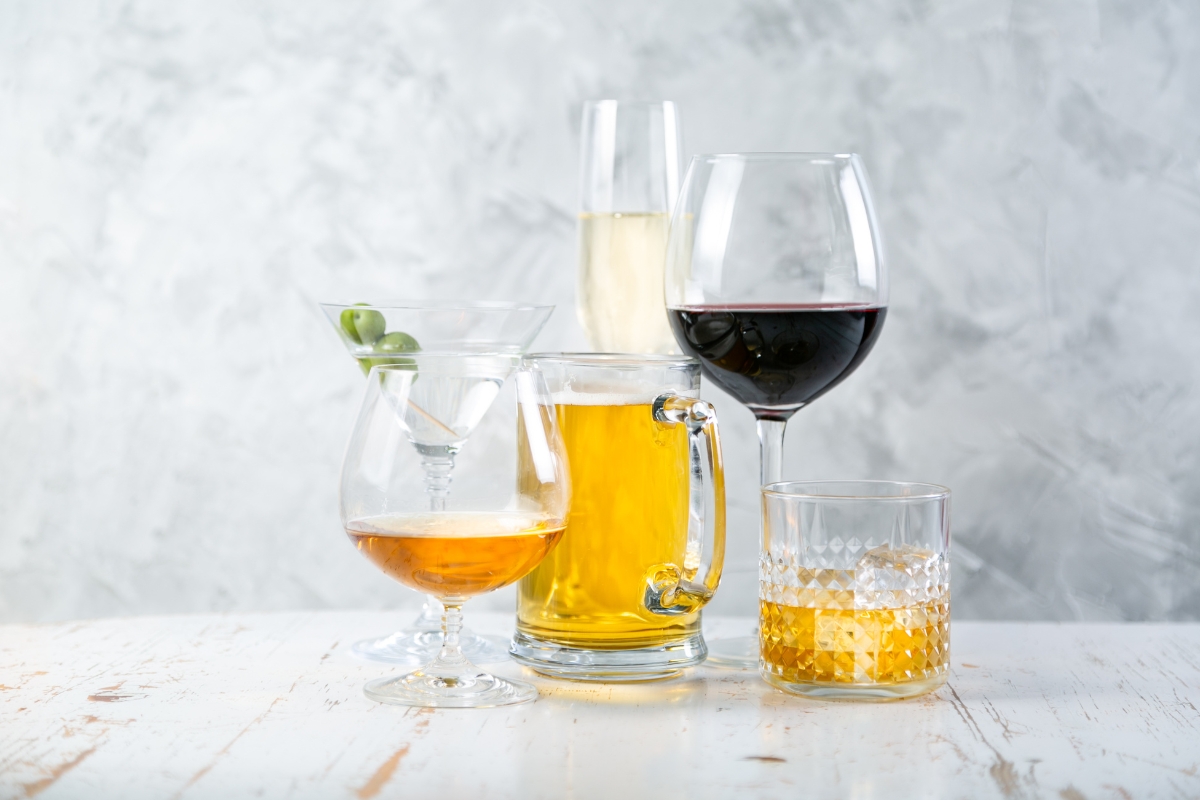 A variety of alcoholic drinks is displayed, including a martini, beer, champagne, red wine, whiskey, and a brandy snifter on a white surface against a light gray background. It's the perfect selection for any eco-conscious catering event.