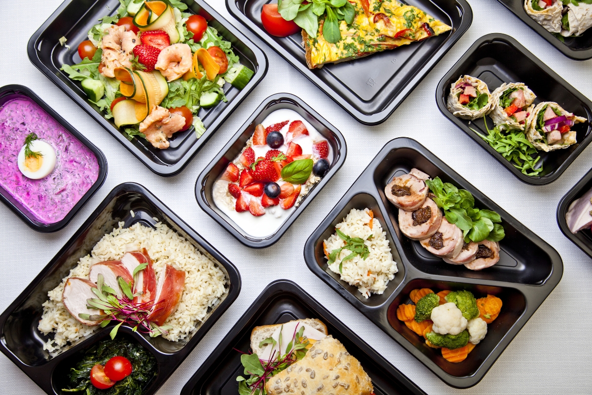 A variety of colorful, pre-packaged meal containers featuring farm-to-table catering options, boasting different food items like salads, fruit, rice dishes, and meats, all arranged beautifully on a white surface.