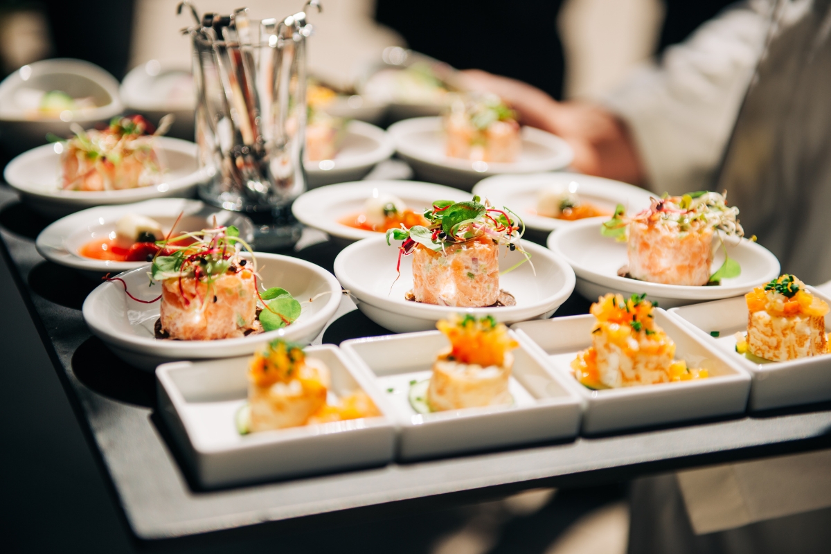 A tray of assorted gourmet appetizers, featuring salmon tartare and bite-sized dishes, elegantly garnished with sprouts and herbs, perfect for custom catering occasions.