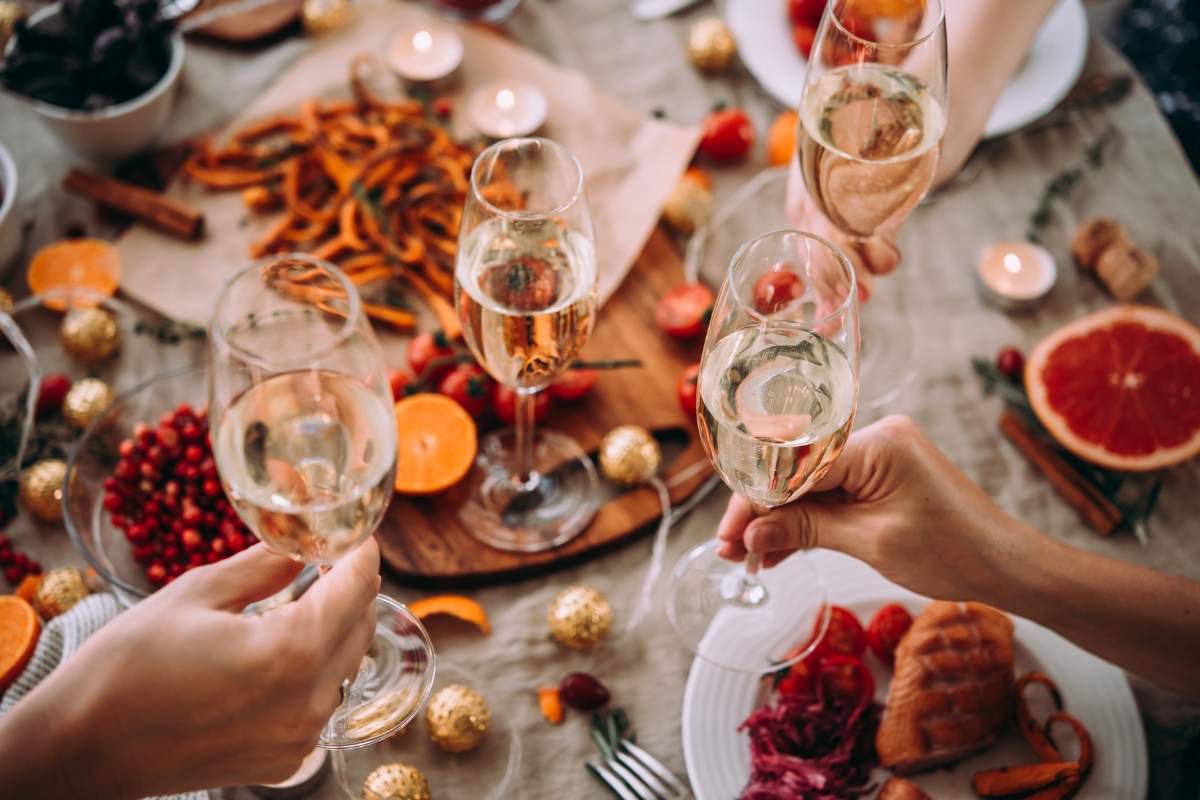 Four hands holding champagne glasses above a festive table laden with fall party food for a crowd, surrounded by candles and decorations.