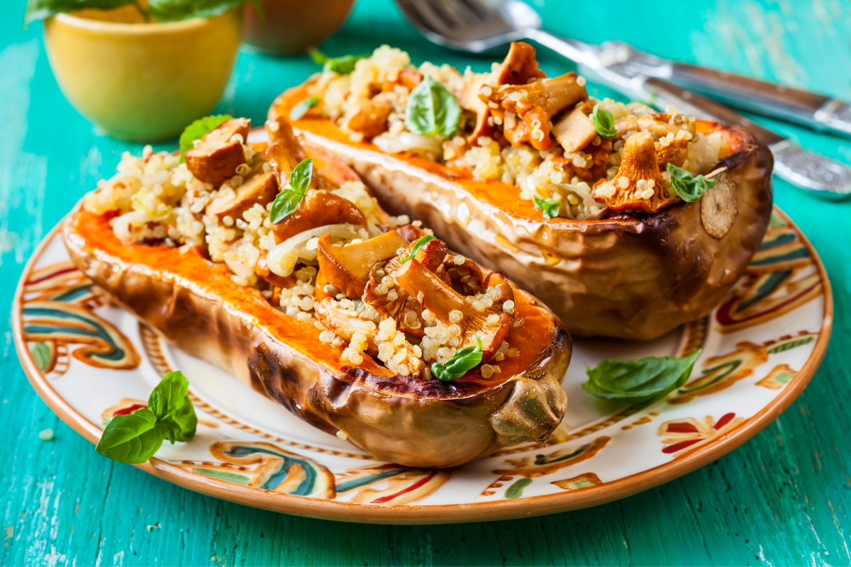 Stuffed butternut squash with quinoa, mushrooms, and basil makes for perfect fall party food for a crowd, elegantly arranged on a decorative plate atop a turquoise table.