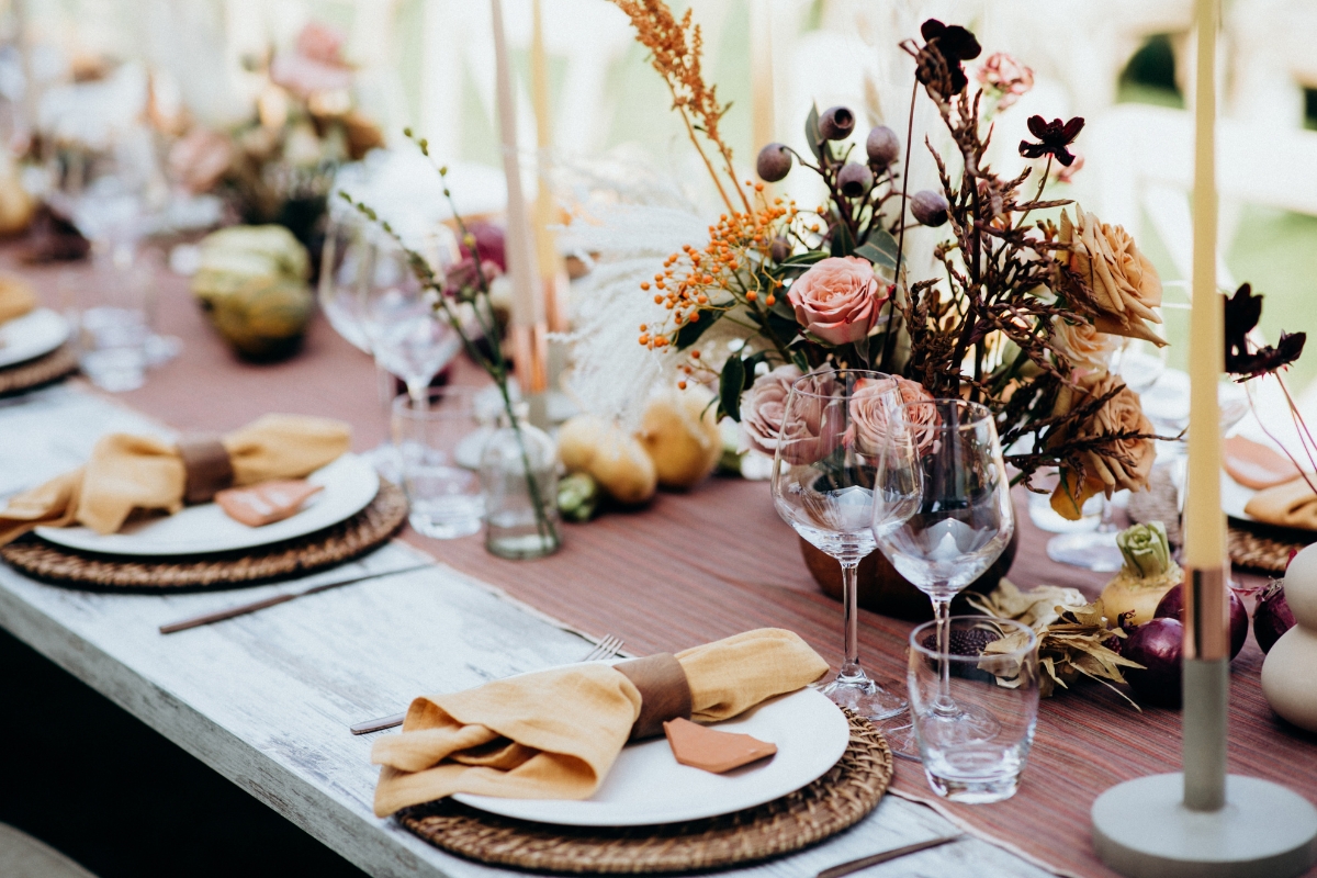 A table setting with elegant dinnerware, glassware, and napkins features floral centerpieces and candles, creating a sophisticated atmosphere perfect for serving fall party food for a crowd.