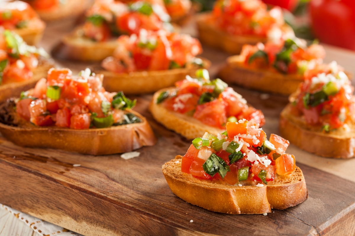 Perfect for a fall party, these slices of toasted bread are topped with diced tomatoes, green onions, and grated cheese on a rustic wooden board—ideal for serving a hungry crowd.