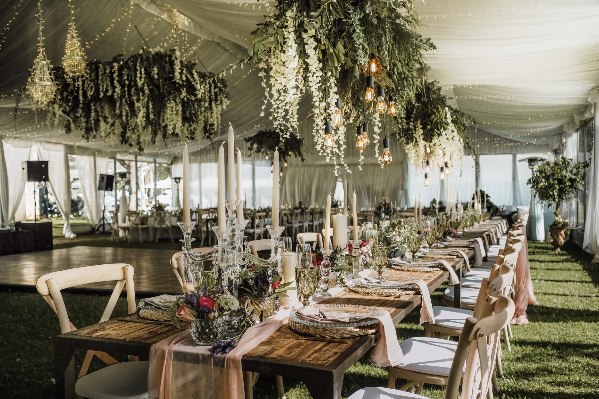 Elegant wedding reception setup in a tent with long tables, floral centerpieces, hanging greenery, and soft lighting—perfectly executed by skilled event planning professionals.