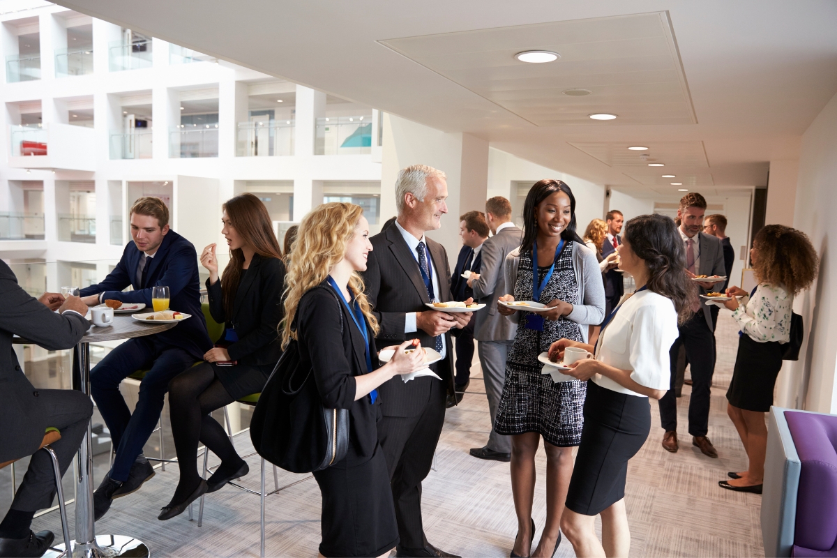 How To Choose The Right Vendor For Your Corporate Event Needs 3 Amidst a modern office setting, professionals in business attire are socializing and enjoying light bites at a networking event, where discussions on how to choose the right vendor seamlessly weave into their conversations.