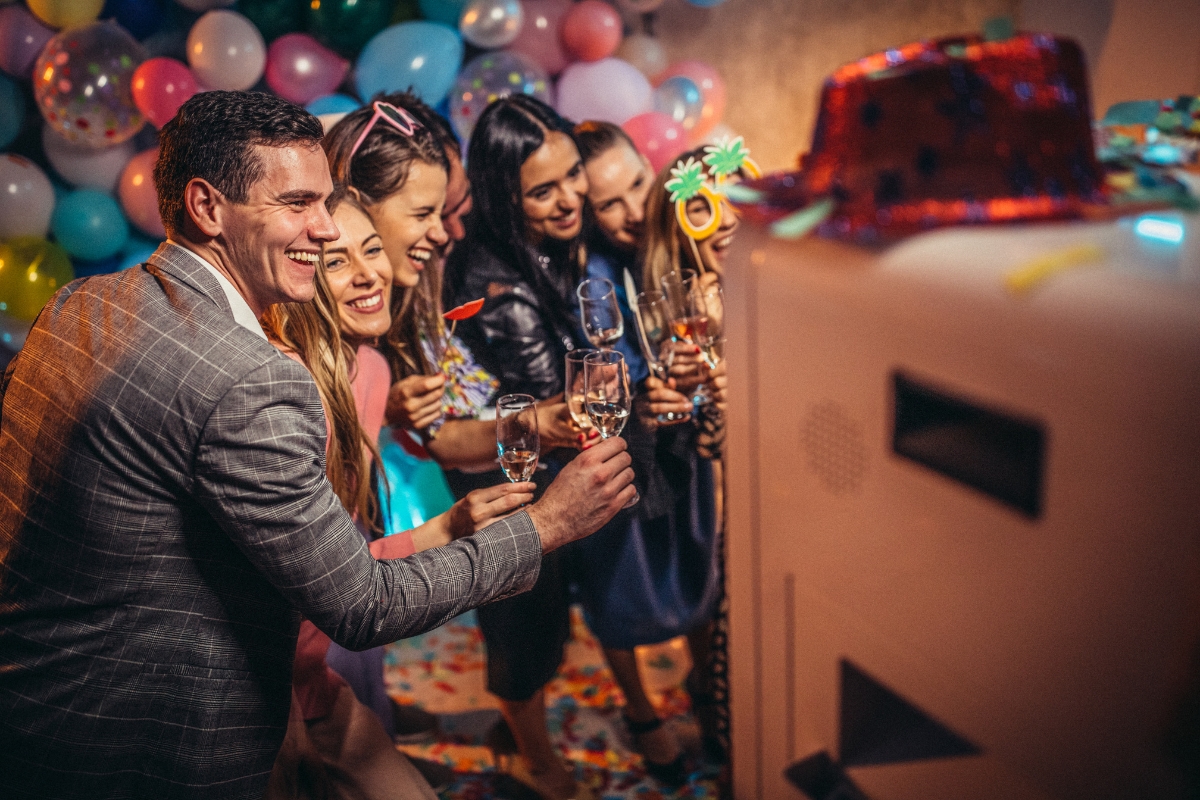 Catering for Graduation Parties Made Easy: Stress-Free Planning Tips 7 A group of people poses and smiles for a photo in front of a photo booth at a festive party with balloons, confetti, and top-notch catering for graduation parties.