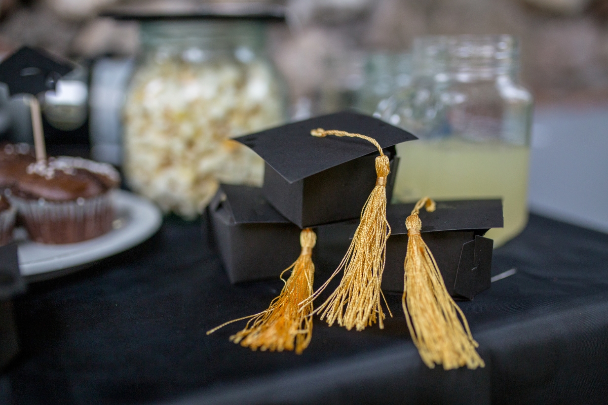 Catering for Graduation Parties Made Easy: Stress-Free Planning Tips 8 Close-up of three black graduation cap decorations with gold tassels on a black tablecloth, featuring popcorn, lemonade, and cupcakes in the background—perfect inspiration for catering for graduation parties.