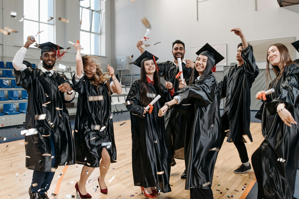 Catering for Graduation Parties Made Easy: Stress-Free Planning Tips 1 A group of graduates in caps and gowns celebrate indoors, smiling and tossing confetti on a gymnasium floor, while enjoying delicious treats from catering for graduation parties.