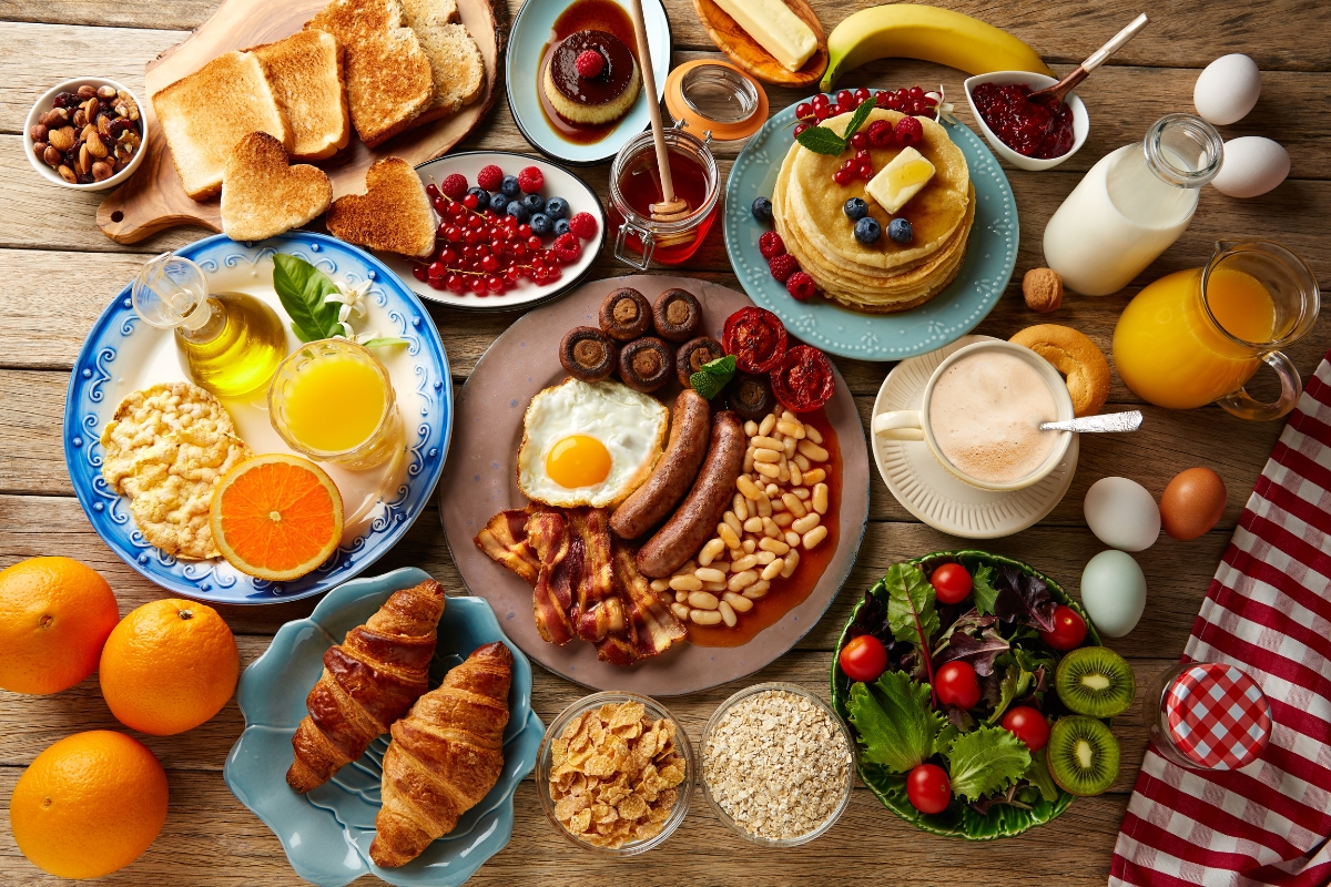 Father's Day Catering: Menu Ideas to Honor Dad 2 A variety of breakfast foods on a wooden table, including eggs, toast, pancakes, fruit, salad, croissants, cereal, juice, milk, and coffee—perfect for Father's Day Catering.