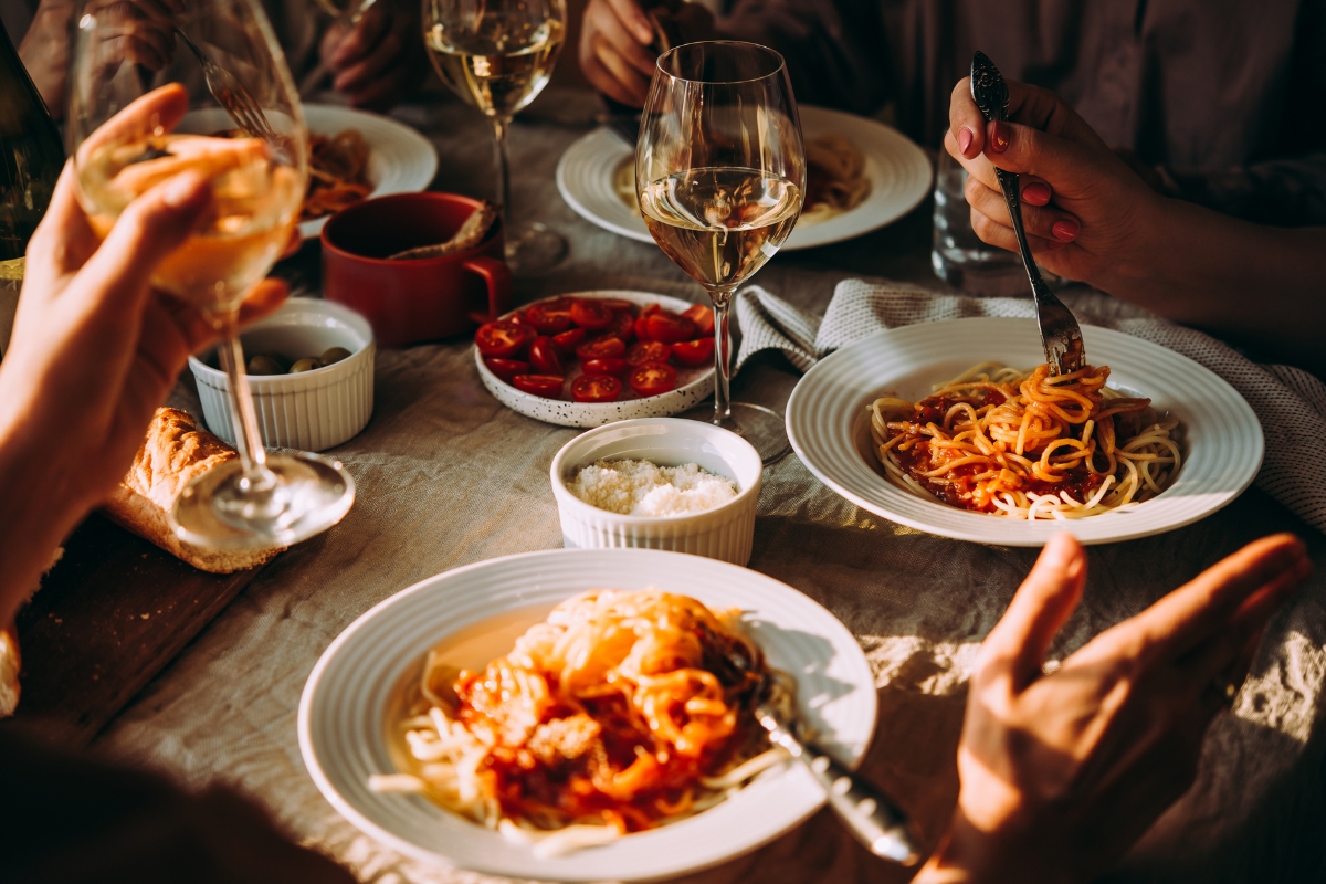 Father's Day Catering: Menu Ideas to Honor Dad 3 People enjoying spaghetti with tomato sauce at a table set with wine glasses, bread, sliced tomatoes, and small bowls of olives and cheese—perfect for a Father's Day Catering celebration.