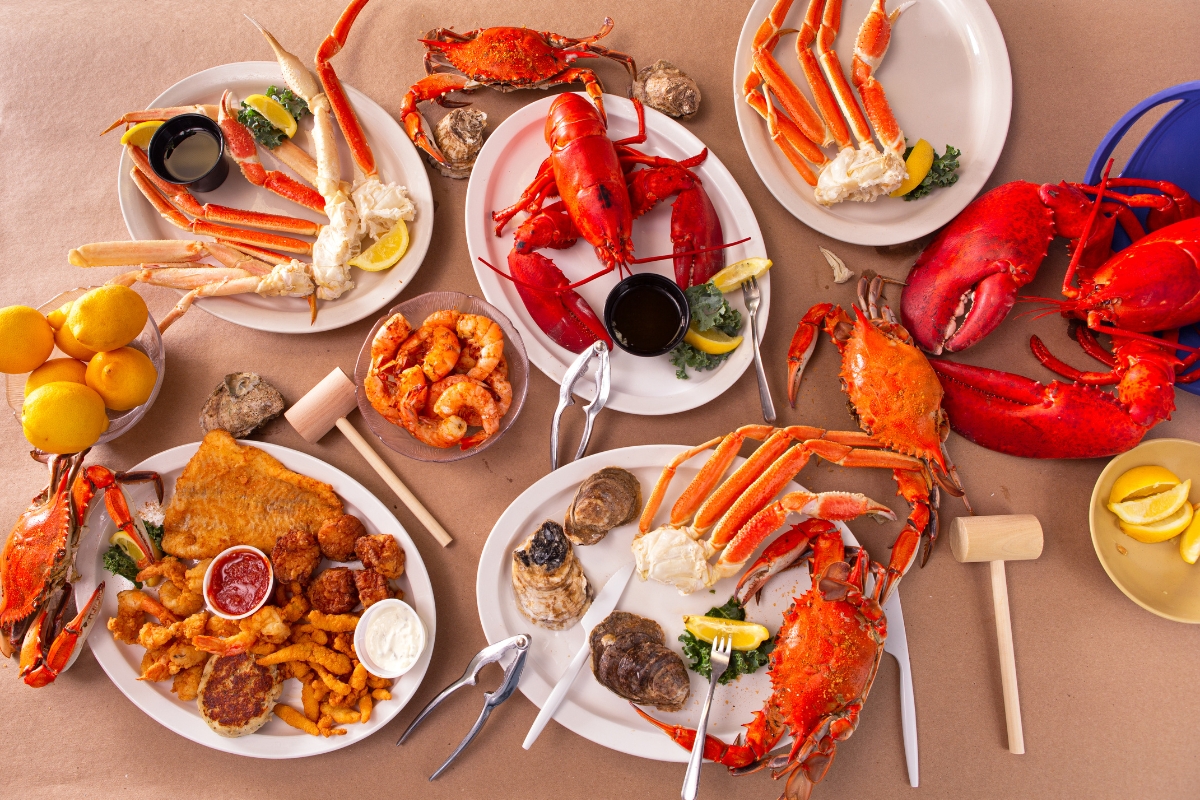 Father's Day Catering: Menu Ideas to Honor Dad 4 Assorted seafood dishes, perfect for Father's Day Catering, including crab legs, lobster, shrimp, oysters, fried fish, lemons, and dipping sauces are arranged on a table with wooden mallets and crackers.