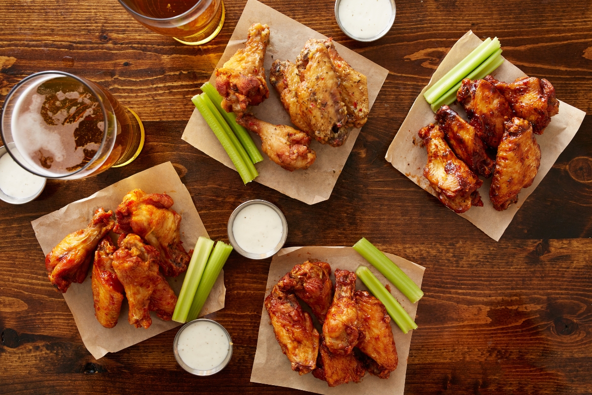 Father's Day Catering: Menu Ideas to Honor Dad 5 Four plates of chicken wings with celery sticks, ranch dipping sauce, and glasses of beer on a wooden table—perfect for Father's Day Catering.