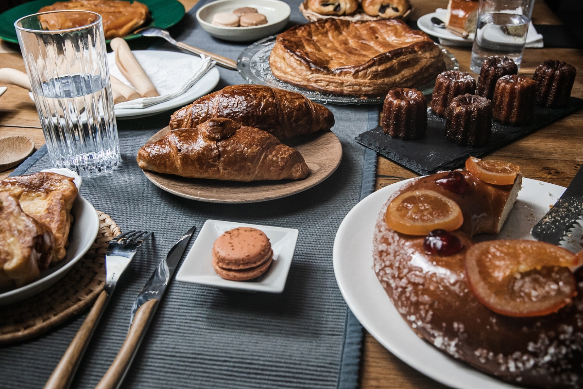 Father's Day Catering: Menu Ideas to Honor Dad 6 A table set for Father's Day Catering features assorted pastries, including croissants, galettes, canelés, a macaron, and a glazed cake, served with glasses of water and cutlery.