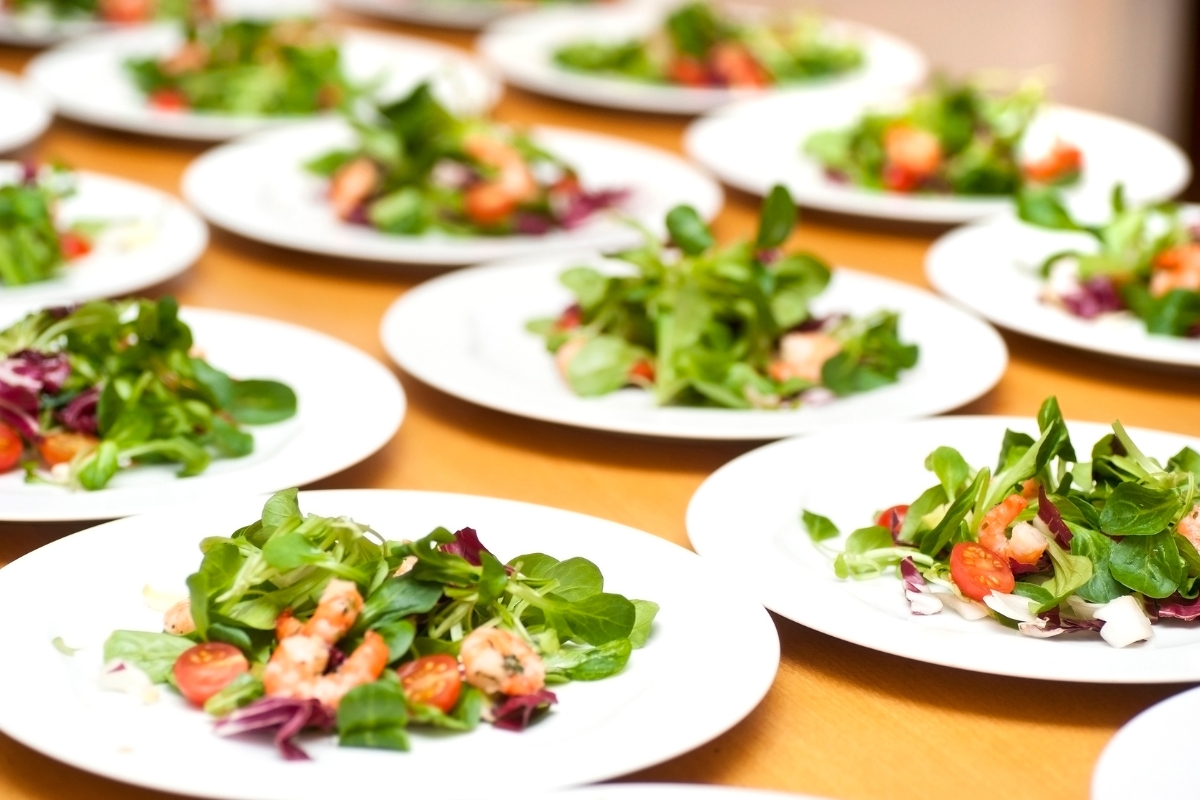 Healthy Catering Options: Light and Fresh Menus for Summer Events 2 Several plates with mixed green salads topped with shrimp and cherry tomatoes are arranged on a table, showcasing delicious and healthy catering options ready to be served.