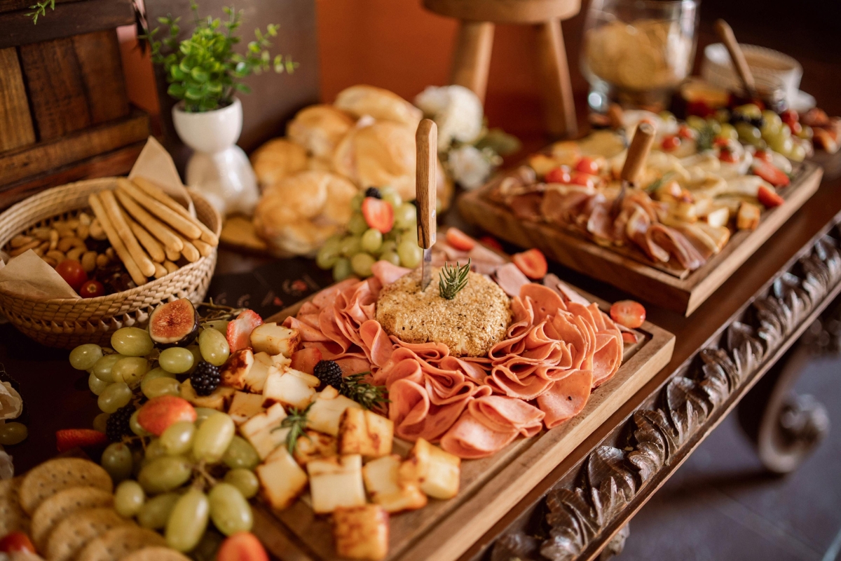 Healthy Catering Options: Light and Fresh Menus for Summer Events 4 A wooden table displays assorted charcuterie boards with sliced meats, cheeses, grapes, crackers, bread rolls, and fruit—perfect for those seeking healthy catering options.