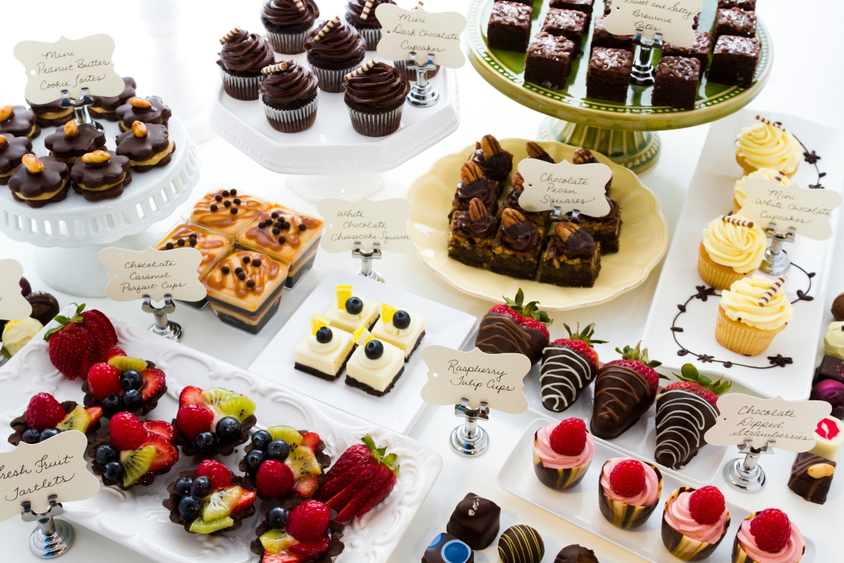 Healthy Catering Options: Light and Fresh Menus for Summer Events 7 Assorted desserts are displayed on platters and cake stands, including cupcakes, brownies, fruit tarts, and mini cheesecakes—each labeled with a handwritten card—offering delightful treats among healthy catering options.