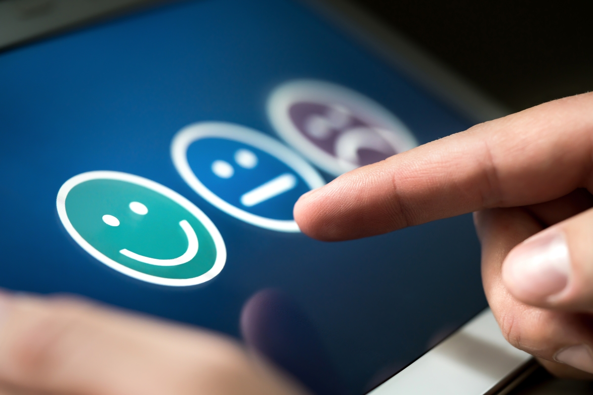 Creating a VIP Catering Experience at Summer Music Festivals 10 A finger touches a digital tablet screen displaying three face icons representing happy, neutral, and sad emotions for a feedback survey at summer music festivals.
